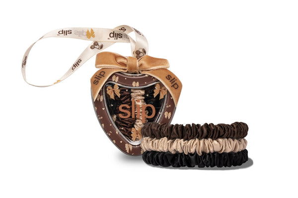 A Slip brand hair accessory set featuring a decorative heart-shaped tin with a ribbon hanger and three stacked scrunchies in dark brown, blonde, and black, shown on a white background.