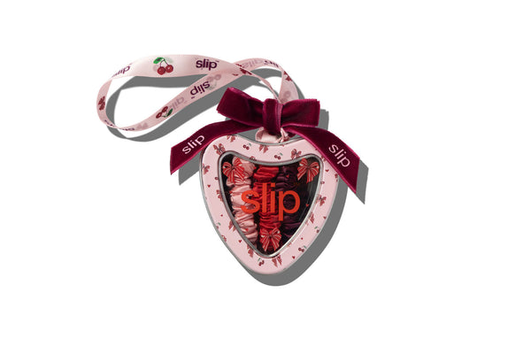 A heart-shaped Slip tin ornament with a pink cherry patterned body, a dark red ribbon bow, and a matching pink cherry-patterned hanging ribbon, shown on a white background.