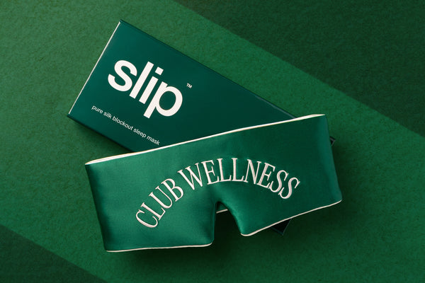 Green silk blockout sleep mask with slip branded packaging on a green background