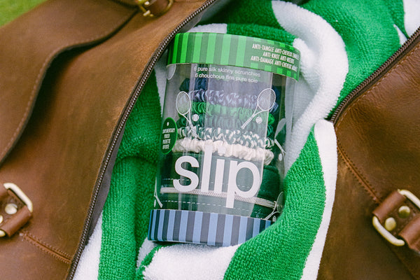 Clear slip container holding silk scrunchies with green lid inside a brown leather bag with a green towel.