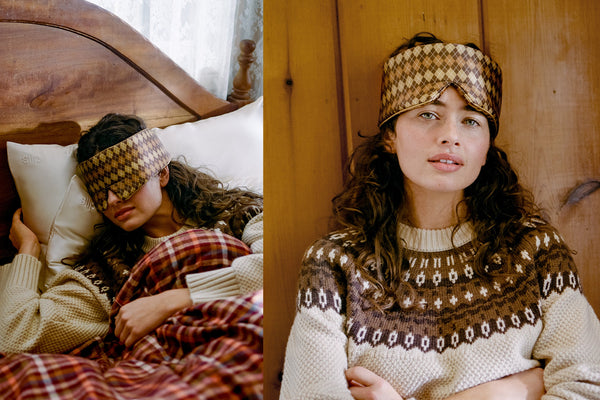 A split lifestyle image showing a woman wearing a brown and beige patterned silk blockout sleep mask while sleeping in bed on the left, and wearing the matching knit sleep mask with a brown and beige sweater against a wooden wall on the right.