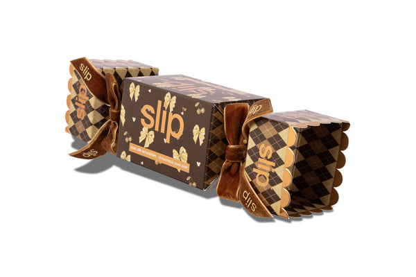 A brown and gold cracker box for slip scrunchies with the brand name 'slip' printed on the front and ends, tied with a matching brown ribbon, shown on a white background.