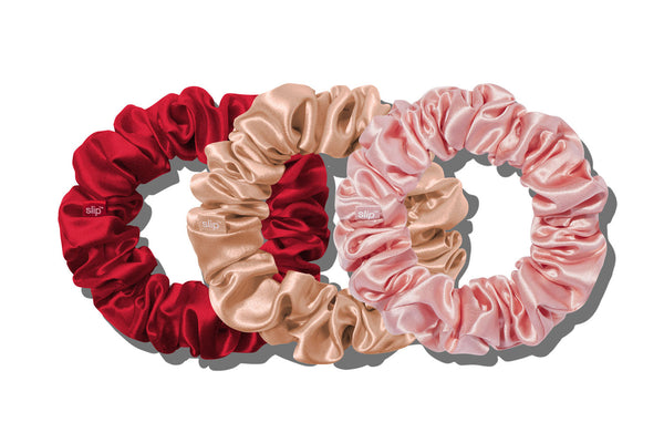 Three slip silk large hair scrunchies in red, peach, and light pink, arranged overlapping on a white background.