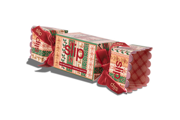 A Christmas-themed silk scrunchie cracker package with a festive patterned design, red ribbons, and the brand name 'slip' visible on the sides, photographed on a clean white background.