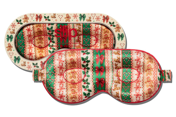 Holiday themed contour sleep mask with a festive Christmas pattern of gingerbread men, ornaments, and snowflakes in red, green, and peach, shown on a plain white background.