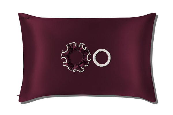 A slip silk queen pillowcase in crimson with two slip silk scrunchies displayed against a clean white background.
