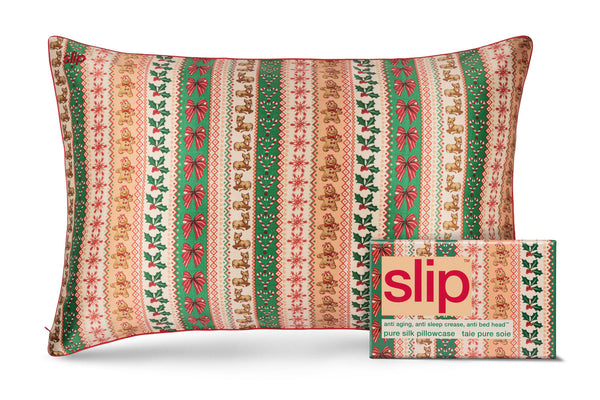 A slip silk pillowcase with a festive vertical knit-style holiday pattern in green, red, beige, and cream, shown next to its matching branded slipcase. The pattern features gingerbread men, holly, bows, and snowflakes.