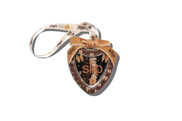A heart-shaped decorative tin ornament with a ribbon hanger, featuring a bow design and slip branding.