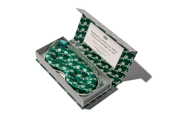 Green silk contour sleep mask in an open box with a slip label on a white background