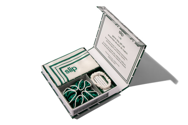 Open box containing a white silk pillowcase, a green silk large scrunchie and a small skinny white scrunchie with 'slip' branding on a white background